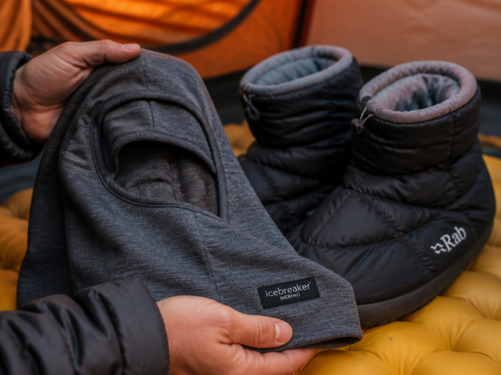 Essential winter camping gear for warmth: balaclava and booties on a sleeping pad.