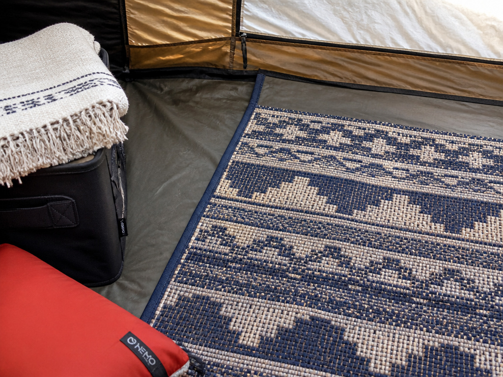 Practical tent textiles: flat-weave rug, gear bin with throw, and camping pillow.